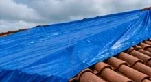 Blue protective tarp secured over a damaged residential tile roof